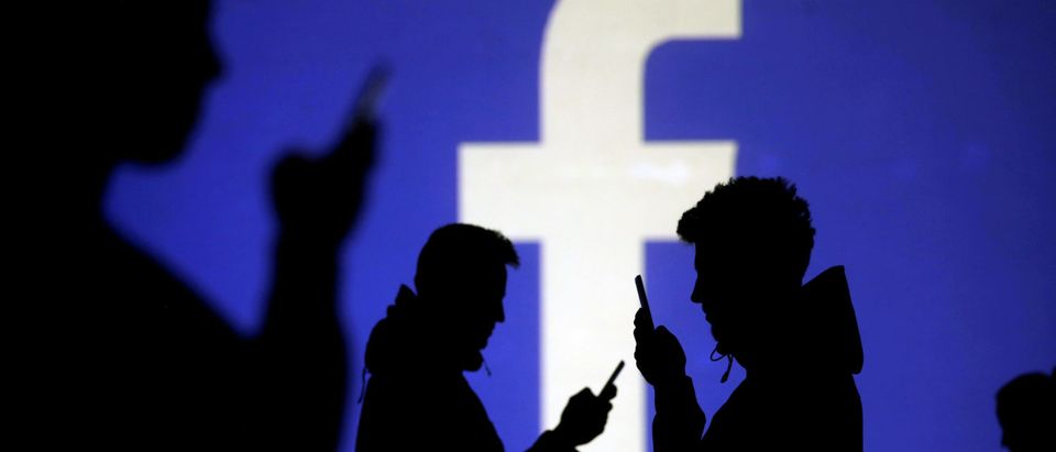 Silhouettes of mobile users are seen next to a screen projection of Facebook logo in this picture illustration taken March 28, 2018. REUTERS/Dado Ruvic