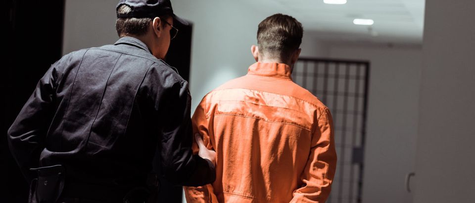 Pictured is a rear view of a prison officer leading a prisoner in handcuffs. Shutterstock