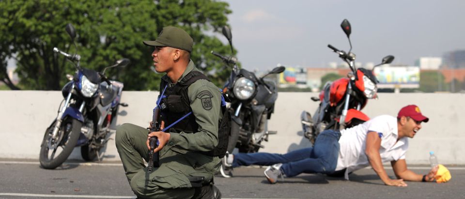 A military member and a man take cover near the Generalisimo Francisco de Miranda Airbase "La Carlota", in Caracas, Venezuela April 30, 2019. REUTERS/Manaure Quintero
