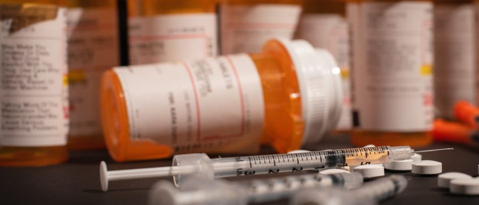 A bottle of prescription medications sits by a syringe. Shutterstock image via Darwin Brandis