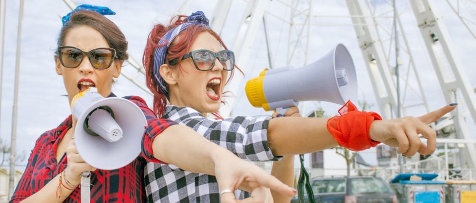 Female protesters at workers day rally shouting political slogans with megaphone loudspeakers wearing red. concept of activism defending jobs and workers rights. (pixelrain/Shutterstock.com)