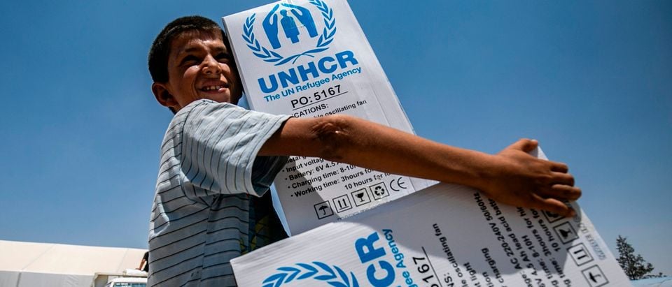 A boy walks carrying packages of humanitarian aid at al-Hol camp for displaced people in al-Hasakeh governorate in northeastern Syria on July 22, 2019, as people collect U.N.-provided humanitarian aid packages. (Photo by Delil souleiman / AFP/Getty Images)