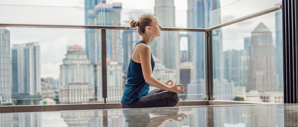 Young woman is practicing yoga in the morning on her balcony with a panoramic view of the city and skyscrapers