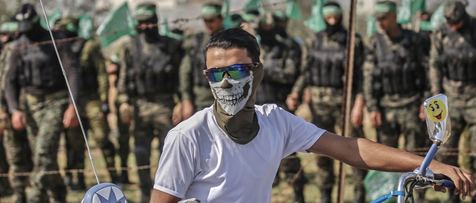 A Palestinian youth covering his face with a mask rides his motorbike in front of fighters from the Ezzedin al-Qassam Brigades, the armed wing of the Hamas movement, during an anti-Israel military show in Khan Yunis in the southern Gaza Strip on Nov. 11, 2019 to mark one year since comrade Nour Baraka, a commander in the group, was killed in an Israeli military operation in the Gaza Strip. (Photo: SAID KHATIB/AFP via Getty Images)