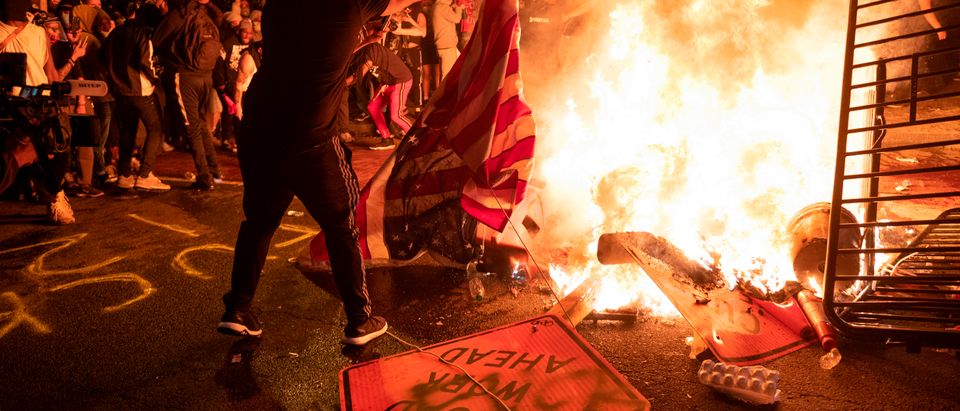 A protester throws a US flag into a burning barricade during a demonstration against the death of George Floyd near the White House on May 31, 2020 in Washington, DC. - Thousands of National Guard troops patrolled major US cities after five consecutive nights of protests over racism and police brutality that boiled over into arson and looting, sending shock waves through the country. The death Monday of an unarmed black man, George Floyd, at the hands of police in Minneapolis ignited this latest wave of outrage in the US over law enforcement's repeated use of lethal force against African Americans -- this one like others before captured on cellphone video. (Photo by ROBERTO SCHMIDT/AFP via Getty Images)