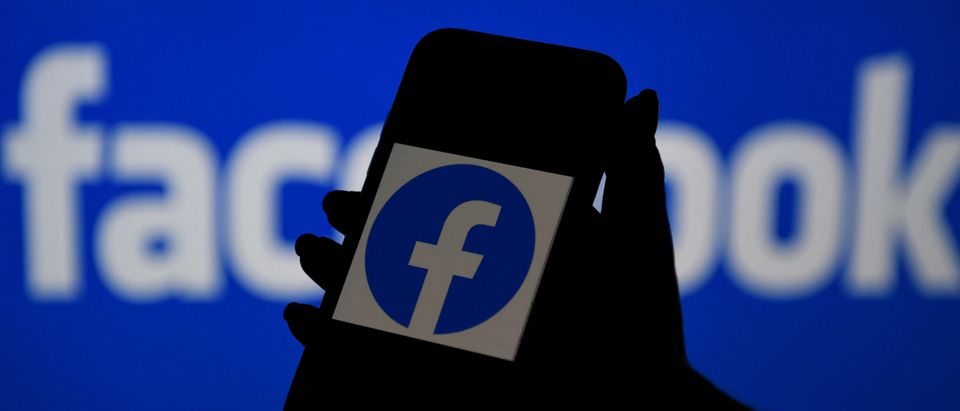 In this photo illustration, a smart phone screen displays the logo of Facebook on a Facebook website background, on April 7, 2021, in Arlington, Virginia - Facebook usage has held steady in the United States despite a string of controversies about the leading social network, even as younger users tap into rival platforms such as TikTok, a survey showed Wednesday. (Photo by Olivier Douliery/AFP via Getty Images)