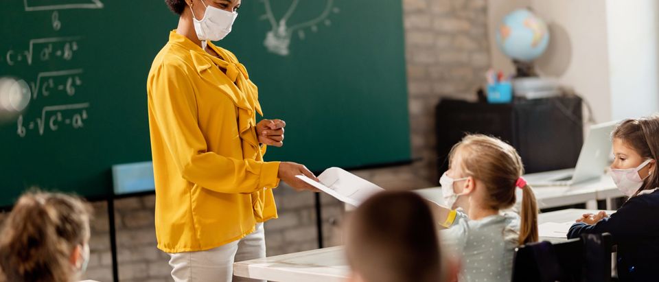 Teacher hands student a note in a classroom. [Drazen Zigic/Shutterstock/