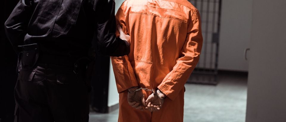 Rear,View,Of,Prison,Officer,Leading,Prisoner,In,Handcuffs,In