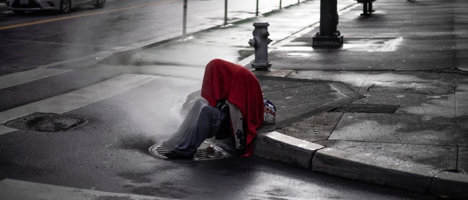 A homeless person sits by a corner as steam emerges from a vent in downtown San Francisco, California