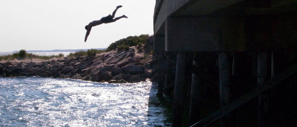 A boy jumps off a bridge into the waters