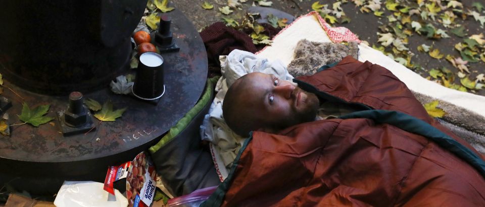 A homeless man stares while laying in his sleeping bag on a sidewalk in Portland, Oregon