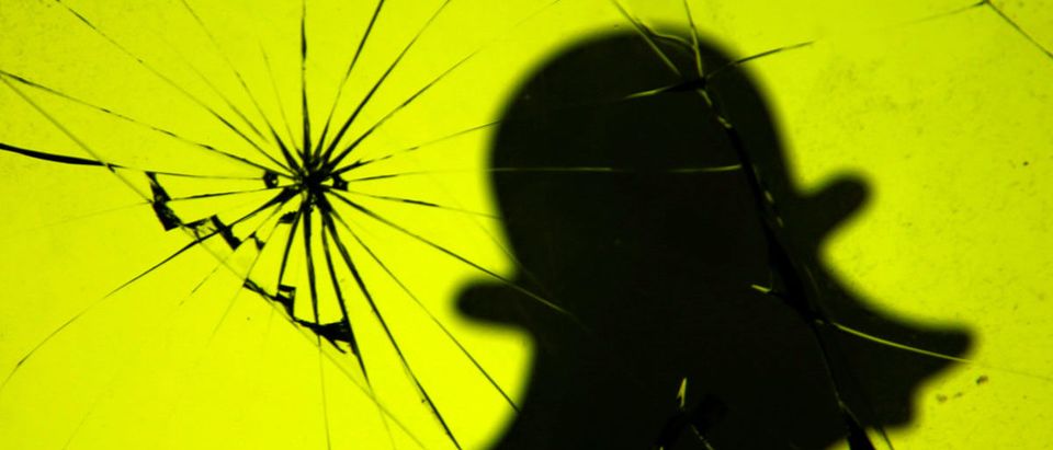 Illustration photo of a 3D printed Snapchat logo is seen through broken glass