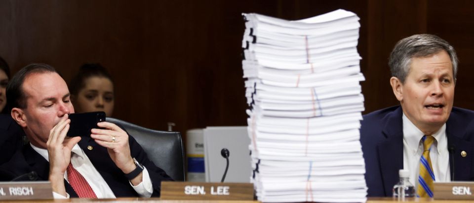 U.S. Senator Mike Lee (R-UT) leans back to take a picture of a stack of regulatory documents displayed by Senator Steve Daines (R-MT) during a Senate Energy and Natural Resources Committee meeting on Capitol Hill in Washington