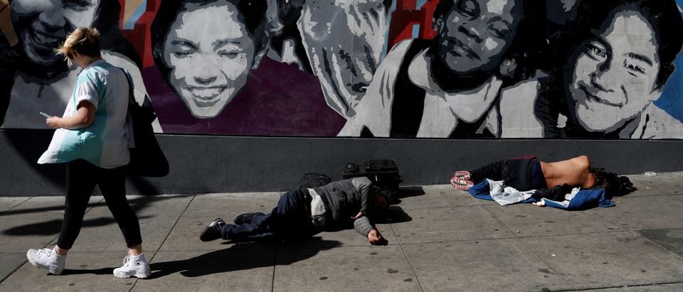 A woman walks past men passed out on the sidewalk n the Tenderloin area of San Francisco, California